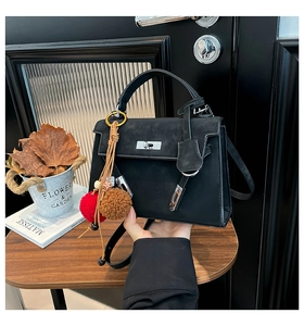 Detail shot of vintage black Kelly bag with fuzzy ball charm on textured wooden table