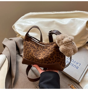 Detail of leopard print fabric handbag with brown leather trim and plush animal charm