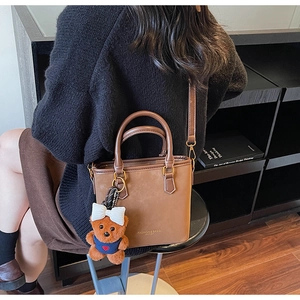 Detailed view of warm brown faux leather tote bag with stylish teddy bear charm