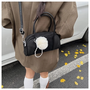 Detail of black cylinder baguette bag with white fur ball and pearl chain strap accents