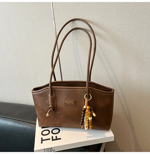 Detail of vintage brown leather tote bag featuring a wooden bead charm and metal logo