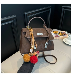 Detail of dark brown faux suede handbag with silver twist lock and colorful pom-poms