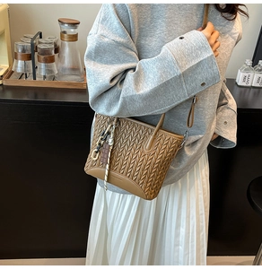 Detailed close-up of brown woven texture crossbody bucket bag with decorative charms