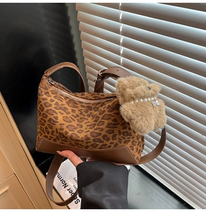 Detail of leopard print crossbody bag featuring brown leather trim and a teddy bear charm