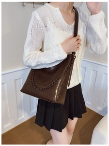 Detail of dark brown leather tote featuring decorative chain and adjustable strap