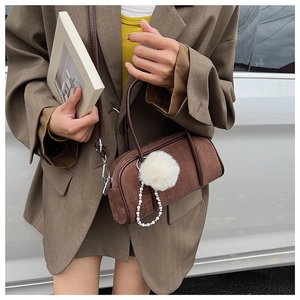 Brown suede bowling bag with fluffy pom-poms and pearl chain detail worn by model