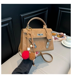 Detailed close-up of brown leather handbag with a colorful pom-pom charm accessory