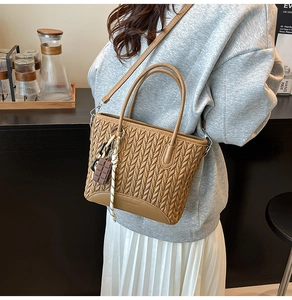 Detail of brown quilted bucket bag with V-shaped texture and decorative chocolate charm