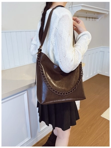 Detail shot of a dark brown glossy bucket bag with thick chain accent on a model