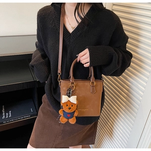 Detail of brown suede tote bag with leather straps and cute plush bear charm