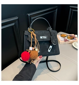 Detail of a black faux suede trapeze bag with silver hardware and a plush charm