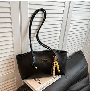 Detail of black leather tote bag with gold logo and colorful wooden bead tassel accessory