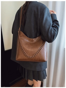 Detail of vintage brown leather hobo bag with matching thick chain decoration on model