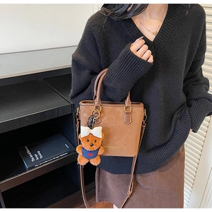 Close-up of brown suede handbag with plush bear charm and fashion leather logo print