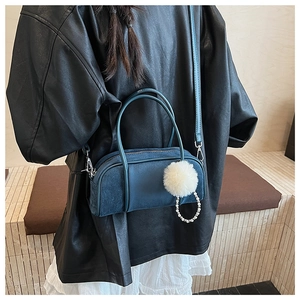 Detailed macro of dark blue velvet bowling bag featuring pearl chain and fluffy pompom