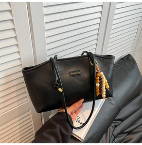 Detail of black faux leather tote bag with gold logo and tricolor wooden bead charm
