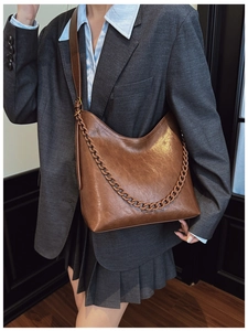 Brown leather hobo bag with thick decorative chain worn over a grey blazer