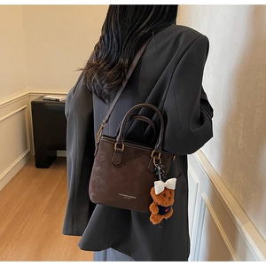 Detail of dark brown matte leather bucket bag with cute plush bear charm accessory