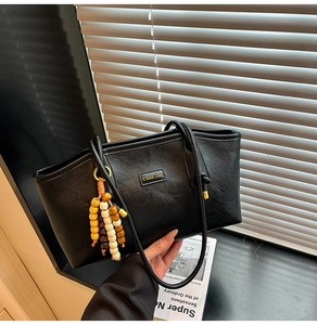 Detail of black leather tote bag with gold brand plate and colorful beaded tassel