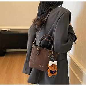 Detail of dark brown suede tote bag with a cute bear charm and adjustable shoulder strap