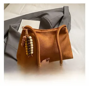 Detail of a brown suede baguette bag featuring a retro colorful wooden bead charm