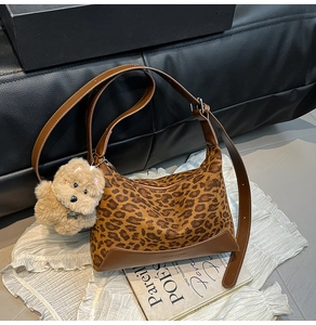 Detail of leopard print half-moon bag with leather trim and plush puppy charm accessory