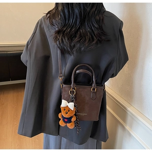 Detailed close-up of dark brown vintage bucket bag with cute bear charm and leather logo