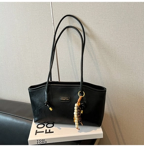 Close-up of black leather tote bag with vintage beads charm and metal nameplate detail