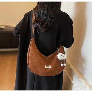 Detail of caramel suede crescent bag featuring a white logo tag and plush cloud charm