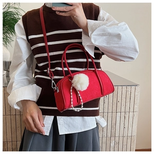 Close-up of red suede bowling bag featuring plush white pom-pom and pearl chain charms