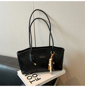 Detail of black leather tote bag with wooden bead charm on a book in minimalist interior