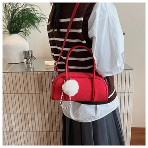 Close-up of a red bowling handbag with white plush ball and pearl chain detail