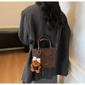 Detail of a brown leather bucket bag with a plush bear charm and detachable shoulder strap