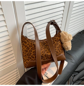 Detailed view of leopard print bag with brown leather trim and cute plush bear charm