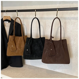 Close-up of matte suede tote bags in caramel, black and brown on a minimalist display