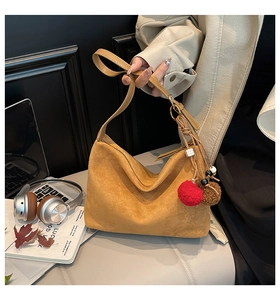 Detail of suede hobo bag in mustard yellow with red pom-pom charm in a lifestyle setting