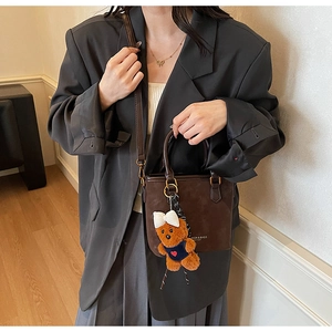 Detail view of a vintage dark brown suede handbag featuring a teddy bear charm and logo