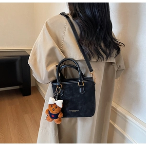 Detail of black leather bucket bag with gold text and cute plush bear charm decoration