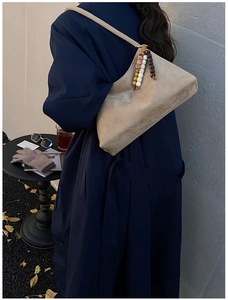 Detail of a beige suede underarm bag with vintage beaded fringe charm on a navy coat