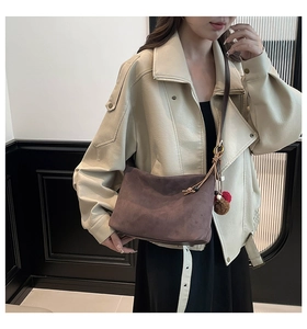 Detail of suede shoulder bag with plush pompom tassel and premium leather strap