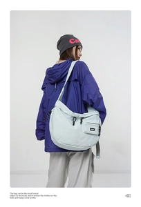 Détail d'un grand sac bandoulière bleu clair en nylon avec cordon sur une veste violette
