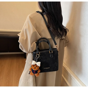 Detail of black crossbody bucket bag with cute brown bear plush pendant and white bow