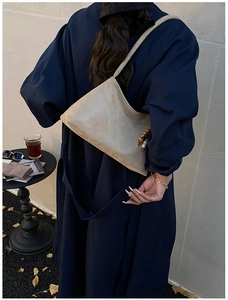 Detail of beige suede shoulder bag with wooden beads on navy trench coat in cafe setting