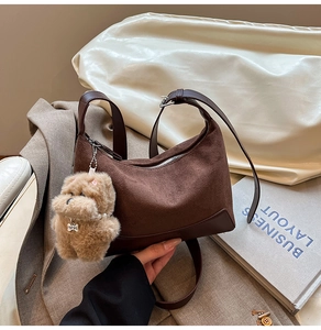 Detail of crescent shoulder bag in brown suede with plush dog charm and leather trim