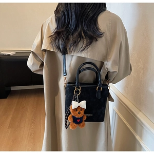 Rear view of a model wearing a black bucket bag with a cute plush bear charm