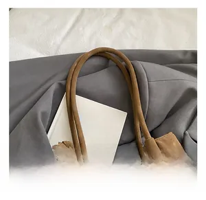 Detail view of large dark brown matte suede tote bag with slim shoulder straps and books