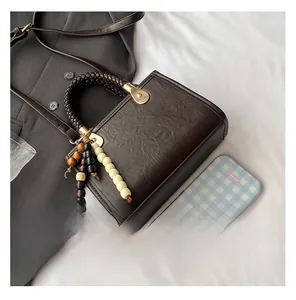 Detailed shot of dark brown leather handbag with woven handle and beaded charm detail