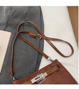 Detail of adjustable leather strap and silver metal buckle on brown suede shoulder bag
