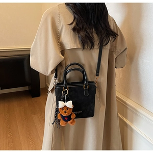 Detail of black leather tote bag with bear charm worn with a stylish trench coat