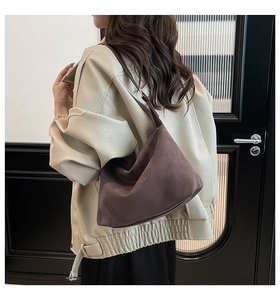 Detail einer dunkelbraunen Hobo-Tasche aus Wildleder, getragen von einem Modell